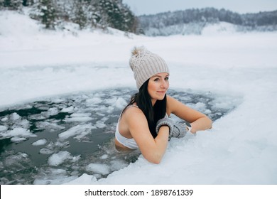 Winter Swimming. Woman In Frozen Lake Ice Hole. Swimmers Wellness In Icy Water. How To Swim In Cold Water. Beautiful Young Female Smiling. Gray Hat And Gloves Swimming Clothes. Nature Lake In Forest