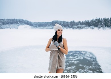 Winter Swimming. Woman Ready To Swim In Ice Water. How To Swim In Cold Water. Beautiful Young Woman Wrapped In A Towel And Swimming Clothes. Gray Hat And Gloves. People And Nature Lake In The Forest.