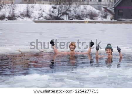 Winter swimming. Young couple ready to swim in ice water. Tea after plunge in cold water.  Ice cold frozen water swimming. Hat and gloves. People and nature lake in the city. Biohacking routine