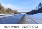 In winter there is snow on the ground, roadsides and branches of spruce trees. The concrete highway among the mixed forests is cleared by road services. Sunny frosty weather and blue sky with clouds