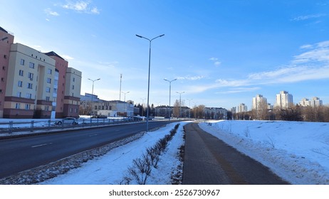 In winter, there is snow on the streets. Tile sidewalks and asphalted driveways are cleared by utilities. Nearby buildings, lamp posts and parked cars. Footprints in the snow. Sunny weather  - Powered by Shutterstock