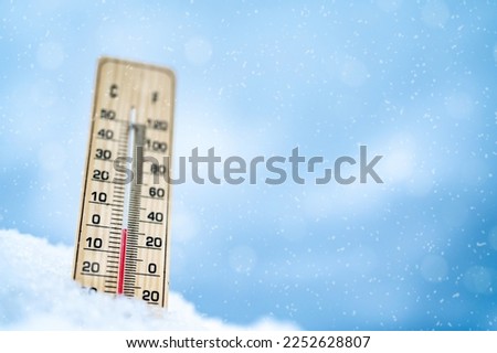 Winter time. Thermometer on snow with blur backround shows low temperatures. celsius and farenheit.