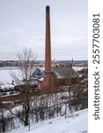 A winter view of an old brick building with a tall chimney, surrounded by snow and trees. This scene captures the essence of Stockholm\