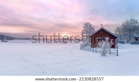 Winter view of a red barn at sunset in Rusko, Finland. Trees covered with snow.