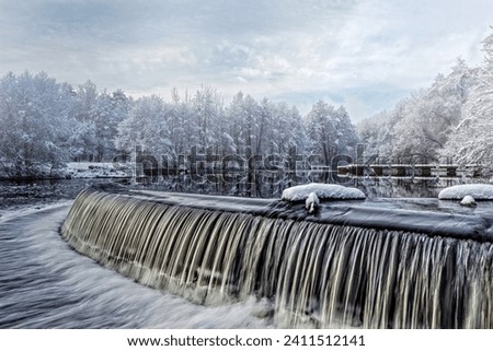 Winter waterscape. Waterfall, snow-covered trees