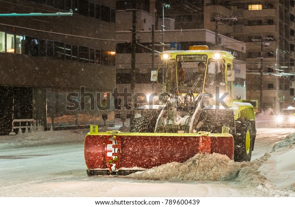 Winter weather, snow on the road, falling\
tree. Snow calamity on the road. Snowstorm in Hokkaido Japan, urban\
road. Snow removal vehicle at work at\
night.