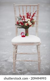 Winter Wedding Bouquet With Pine Cones And Red And White Flowers On A Chair With A Ring