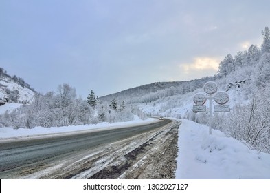 Winter winding  snowy mountain highway leading through a mountain landscape. Evening twilight, road signs covered with snow after a snowfall - the concept of safety in winter driving