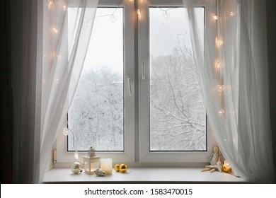 Winter window with white curtains and christmas lights, lantern with toys sitting on window sill 