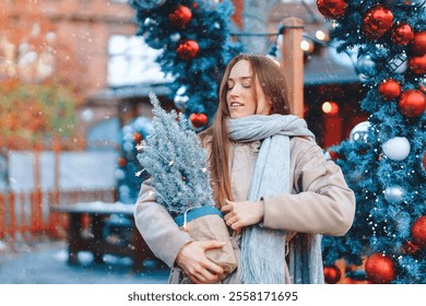 Winter woman holding small tree with decorations in a festive outdoor setting - Powered by Shutterstock