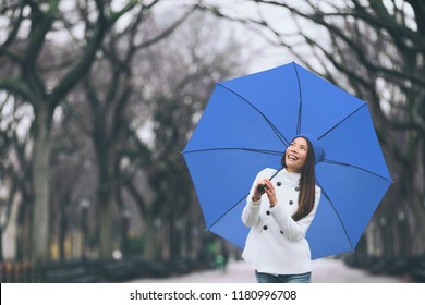 Winter Woman Walking In Snowy Forest Park Enjoying Outdoor With Blue Umbrella For Snow. Asian Girl Happy In Central Park, New York City.