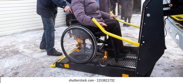 Winter. A woman in a wheelchair on a lift of a specialized vehicle for people with disabilities. Taxi for the disabled. Yellow bar and handrail.