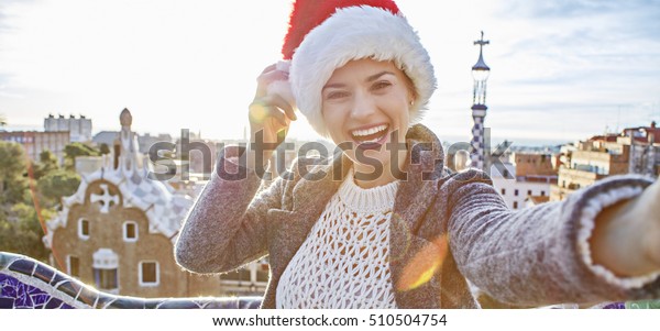 バルセロナの冬のワンダーランド スペイン バルセロナのグエル公園でサンタハットに住む トレンディーなトラベラーウーマンの笑顔のポートレート の写真素材 今すぐ編集