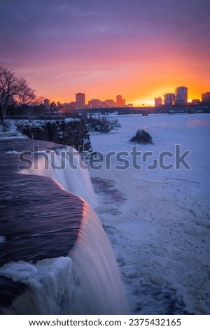 Winter wonderland scenery, frozen waterfall with colourful purple sunset sky, Rideau Falls, Ottawa River, Ottawa (Ontario), Gatineau (Quebec), Canada. Photo taken in January 2022.