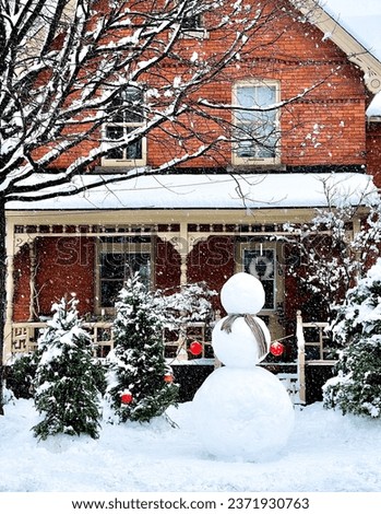 Winter wonderland scenery with snowman in front of charming red brick house with porch and trees on a snowy day, Ottawa, Ontario, Canada. Photo taken in January 2021.