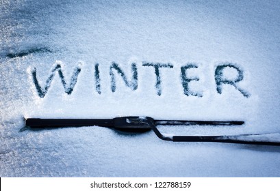 Winter written in snow on car windscreen below windscreen wiper