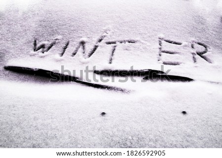 Winter written in snow on car windscreen below windscreen wiper