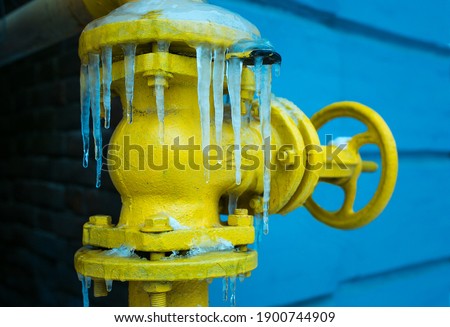 Winter. The yellow gas valve is covered with ice and icicles.