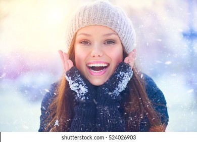 Winter Young Woman Portrait. Beauty Joyful  Model Girl Touching Her Face Skin And Laughing, Having Fun In Winter Park. Beautiful Young Woman Laughing Outdoors. Enjoying Nature, Wintertime