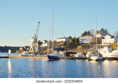 Winterized sloop rigged yachts and cutters moored to a snow-covered pier. Port crane in the background. Norway. Nautical vessel, transportation, sport, recreation, leisure activity, service