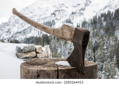 Winterscene of an axe in a chopping block ,with snow,trees and mountains in the back