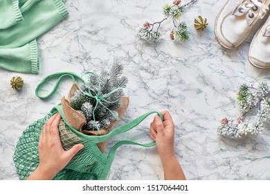 Wintertime, Creative Flat Lay With Artificial Plastic Christmas Tree In Eco Friendly Mesh Bag. Real Or Fake Xmas Tree Dilemma For Eco Friendly People. Flat Lay On Light Stone In Mint Green.