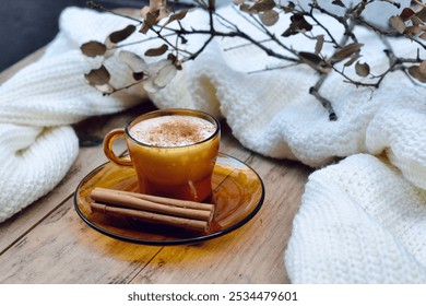 Wintery hot cup of coffee with milk and cinnamon on a rustic wooden table decorated with cinnamon sticks, dried leaves and a woolen sweater. Winter atmosphere - Powered by Shutterstock