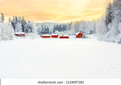 Wintery scene on a woodland homestead with stark contrast between the white snow, orange sunset, and red houses. - Powered by Shutterstock