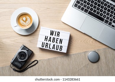 Wir Haben Urlaub Written In German On Light Box Meaning Closed For Holidays As Flatlay From Above Of An Office Desk Background With Laptop Keyboard