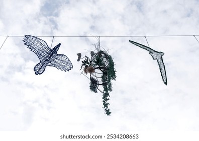 Wire bird sculptures and hanging plants against a cloudy sky - Powered by Shutterstock