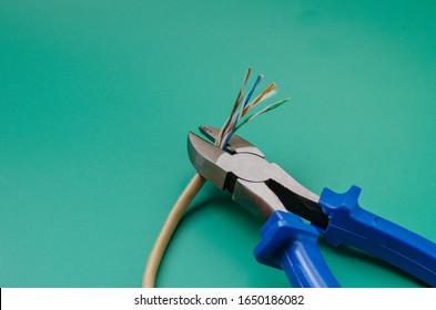 The wire cutters cut the patch cord. Old LAN cable with thin wires without braid. Eye level shooting. Close-up. Selective focus.