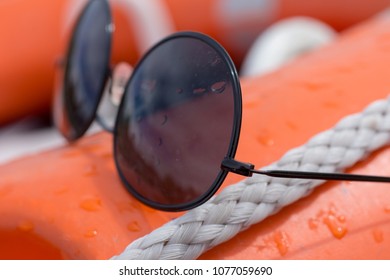 Wire Frame Black Sunglasses Covered In Water Droplets Placed On Board An Orange Boat Buoyancy Aid