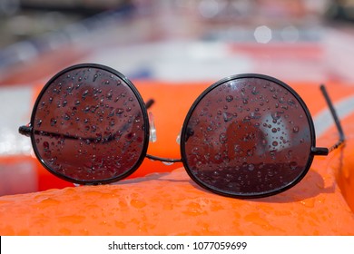 Wire Frame Black Sunglasses Covered In Water Droplets Resting On Board A Boat Buoyancy Aid