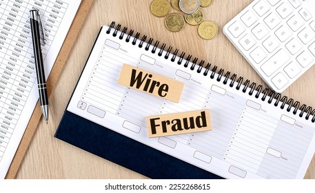 WIRE FRAUD word written on wooden block on planner with coins, clipboard and calculator - Shutterstock ID 2252268615
