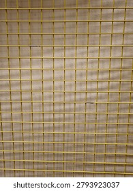 Wire mesh casting shadows on a yellow wall background, creating geometric patterns and textured surfaces suitable for abstract and design concepts.