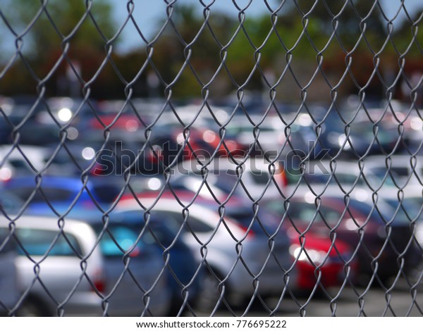 Wire mesh of a full outdoor\
car park or parking lot with blurry view of rows of cars parked\
inside.