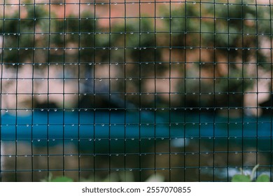 Wire mesh netting soaked from rain, with water droplets hanging on its surface, capturing the aftermath of a rainy day in an industrial or outdoor setting. - Powered by Shutterstock