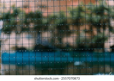 Wire mesh netting soaked from rain, with water droplets hanging on its surface, capturing the aftermath of a rainy day in an industrial or outdoor setting. - Powered by Shutterstock