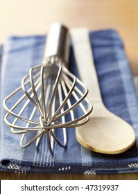 Wire Whisk, Wooden Spoon And Kitchen Towel On A Board.  Shallow Depth Of Field.