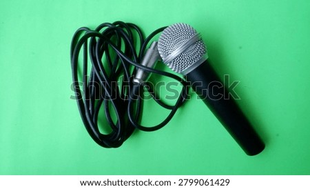 Wired handheld microphone with cable on a green background. Ideal for audio recording, broadcasting, podcasting, music performance, communication, and sound technology concepts.