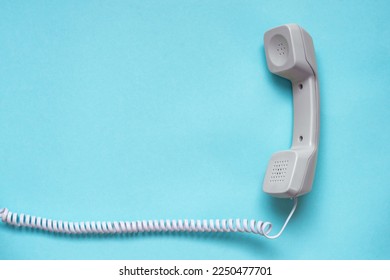 Wired telephone handset on blue background. Telephone handset of a vintage telephone. White telephone receiver on spiral cord on blue background. Negotiation concept. Hot line concept. 
