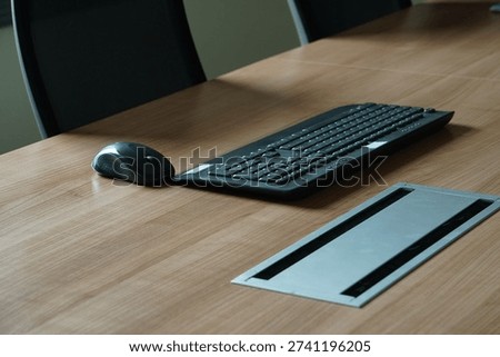 A wireless black mouse and a full-sized keyboard are placed on the wooden desk.
