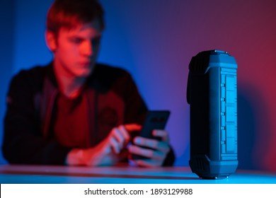 Wireless bluetooth speaker. Column controlled via bluetooth on table. He plays music through his phone. Wireless speaker is controlled by bluetooth technology. Man with phone is blurred in background