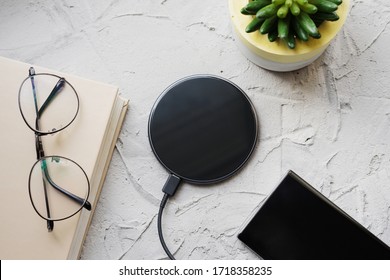 Wireless charging on a gray concrete background with a book, smartphone, glasses and a plant.