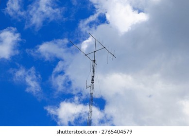 Wireless Communication Antenna Tower with Cloudy Sky Background. An outdoor handheld transceiver (HT) antenna installed on a metal support mast. This image symbolizes modern wireless networking, emergency broadcasting, and long-range radio transmission technology.