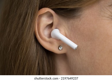 Wireless Earphone Object In Female Ear Close Up. Gadget User Woman Using White Small Earbud, Listening To Music, Talking On Video Phone Call. Cropped Shot. Communication