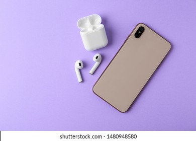 Wireless Earphones, Mobile Phone And Charging Case On Violet Background, Flat Lay. Space For Text