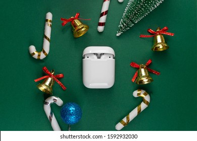 Wireless Headphones On Green Christmas Background. Airpods. Air Pods. With Wireless Charging Case. Entangled 3.5 Headphones. Copy Space