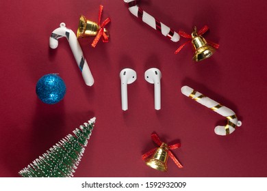 Wireless Headphones On Red Christmas Background. Airpods. Air Pods. With Wireless Charging Case. Entangled 3.5 Headphones. Copy Space