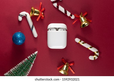 Wireless Headphones On Red Christmas Background. Airpods. Air Pods. With Wireless Charging Case. Entangled 3.5 Headphones. Copy Space